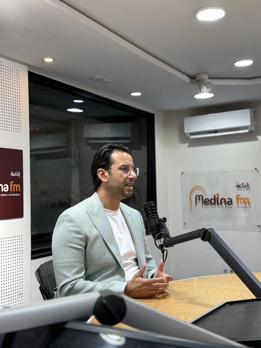 Abdelmajid Charrass en veste bleu clair parlant devant un microphone de radio.