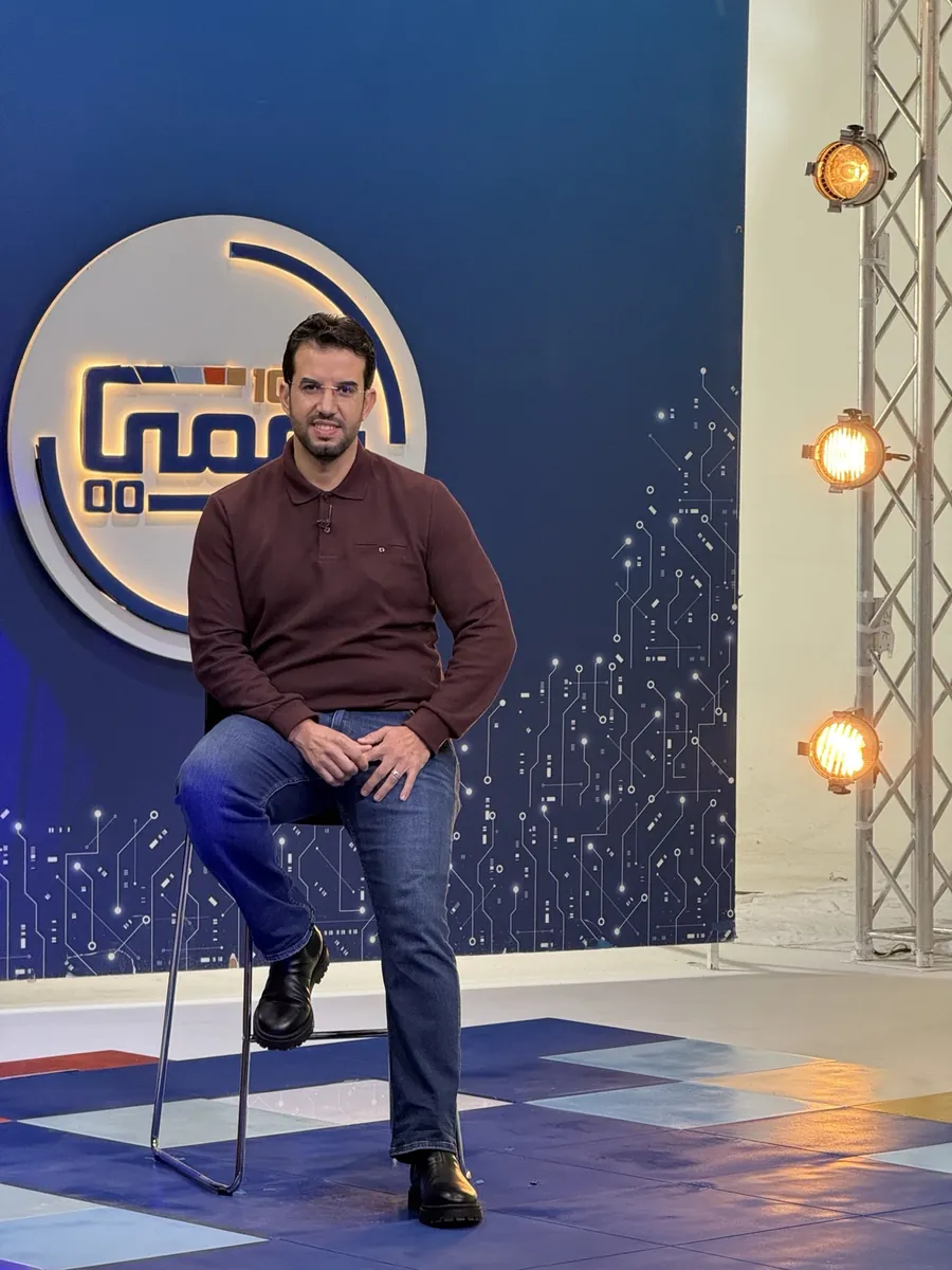 Abdelmajid Charrass assis devant un décor bleu, vetu d’un polo bordeaux.